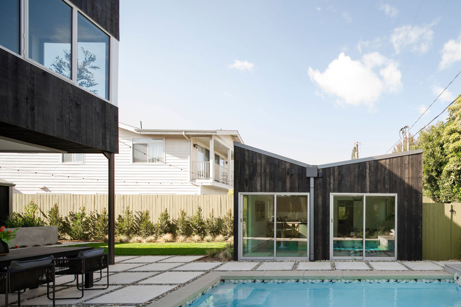 A modern black-clad house beside a pool in daylight.